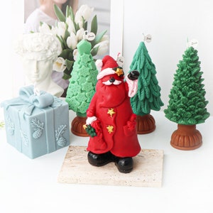 May include: Set of five Christmas-themed candles, including a Santa Claus candle, a gift box candle, and three Christmas tree candles. The candles are made of a red, green, and blue wax.