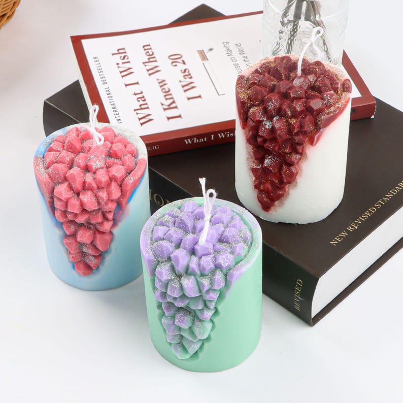 May include: Three pillar candles with a crystal-like design. The candles are in shades of pink, purple, and red. The candles are on a book with the title "What I Wish I Knew When I Was 20".