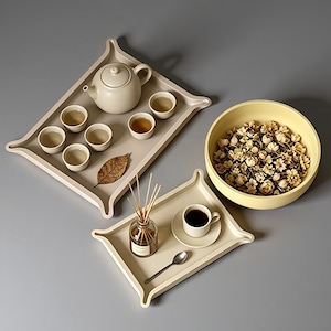 May include: Two rectangular beige trays with raised corners, one holding a teapot and five small cups with a dried leaf, the other holding a reed diffuser, a cup on a saucer, and a spoon. A large yellow bowl filled with dried flowers sits nearby.