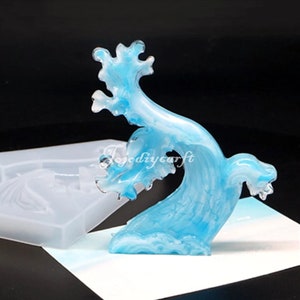 May include: A translucent blue resin wave sculpture with white marbling. The wave is in motion, with a cresting top and a curved base. A silicone mold is visible in the background. The text "Tojodiycraft" is visible on the image.