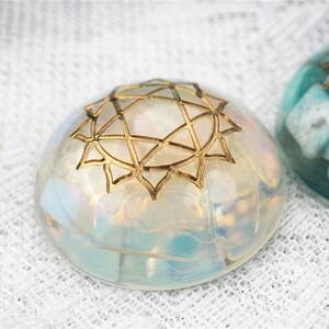 May include: A clear, iridescent glass orb with a gold geometric design on top. The orb is sitting on a white fabric surface.