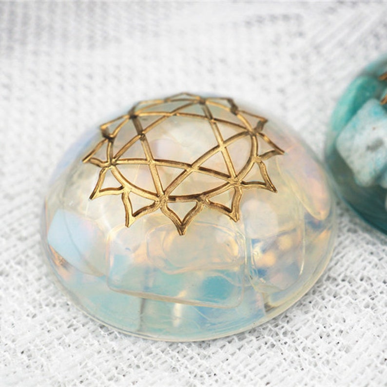 May include: A clear, iridescent glass orb with a gold geometric design on top. The orb is sitting on a white fabric surface.