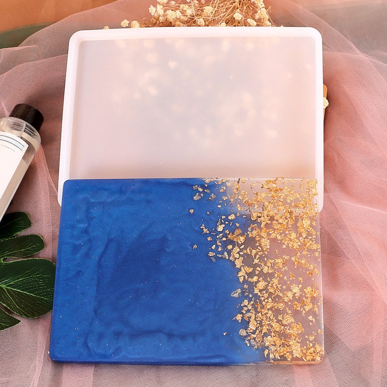 May include: A clear silicone mold for resin casting, with a finished resin piece showing a blue and gold design. The resin piece has a blue base with gold flakes scattered on the right side.