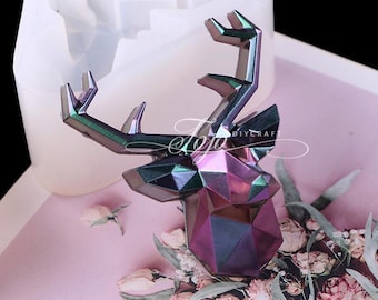 May include: A geometric deer head mold made of silicone. The mold is white and has a detailed design. The deer head is in a geometric style with a purple and green iridescent finish.