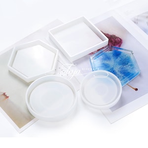 May include: Set of five white silicone moulds for making coasters. The moulds are in different shapes, including round, square, and hexagonal.