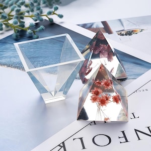 Puede incluir: Tres moldes de resina transparente para manualidades. Un molde cuadrado con fondo puntiagudo y dos moldes en forma de pirámide. Los moldes en forma de pirámide contienen flores secas.