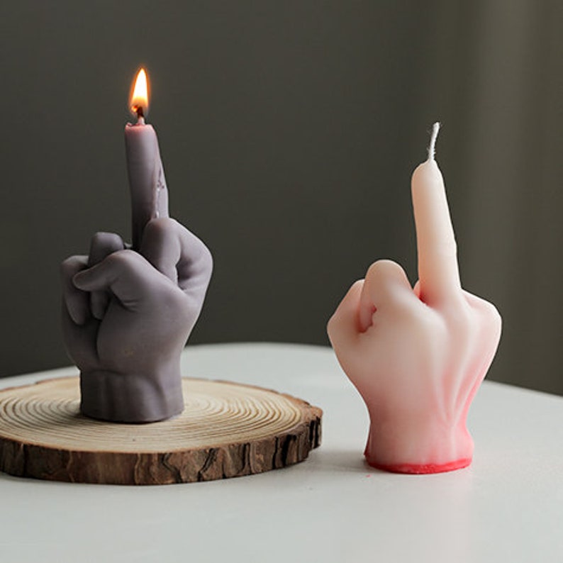Pu&ograve; includere: Due candele a forma di mano, una grigia e una rosa, con il dito medio esteso. La candela grigia &egrave; accesa.