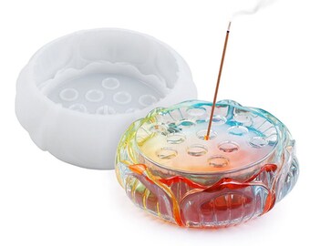 Puede incluir: Un porta incienso de vidrio transparente con un diseño de arcoíris y un molde de silicona para hacer el porta incienso. El porta incienso tiene una base circular con un borde elevado y un agujero central para los palitos de incienso. El molde es blanco y tiene un diseño similar al del porta incienso.