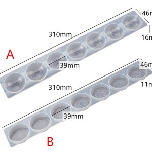 May include: Two clear silicone molds for making resin crafts. Each mold has six round cavities with different designs. The molds are 310 mm long and 46 mm wide. The top mold has cavities that are 39 mm in diameter and 16 mm deep. The bottom mold has cavities that are 39 mm in diameter and 11 mm deep.