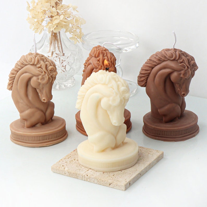 May include: Three horse head candles, one white, one brown, and one dark brown. The candles are on a white surface.