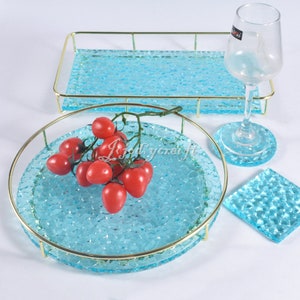 May include: A set of four blue glass trays with gold metal rims. The trays are textured and have a raised pattern. One tray has a cluster of red cherry tomatoes on top.