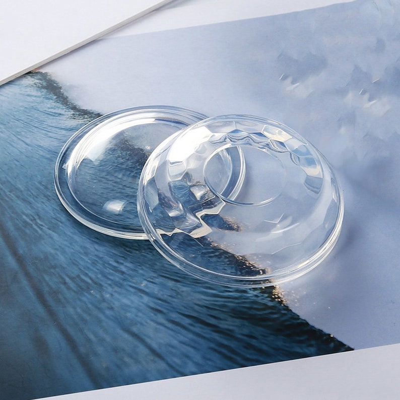 May include: Two clear plastic lids for food containers. The lids are round and have a slightly domed shape. One lid has a smooth surface, while the other has a textured surface.