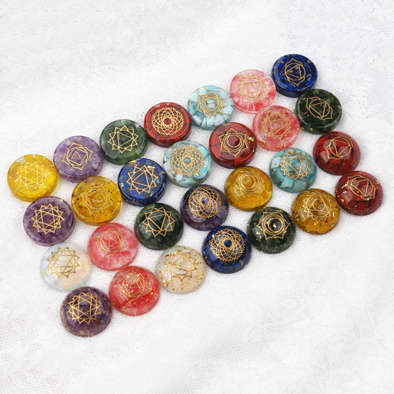 May include: A collection of 20 round, colorful, chakra stones with gold symbols. Each stone has a different color and symbol representing a different chakra.