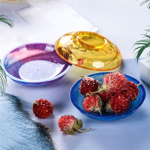 May include: Three resin trays in different colors: purple, yellow, and blue. The blue tray has dried red flowers inside. The trays are round and have a slightly raised edge.