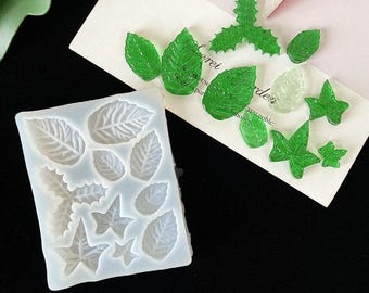 Puede incluir: Un molde de silicona blanco con 12 formas de hojas diferentes. El molde se utiliza para crear artesanías de resina. También hay varias hojas de resina verde en la imagen.