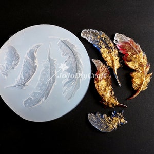 May include: A silicone mold with four feather shapes, and five gold and red glitter resin feathers. The mold is clear and the feathers are shiny.