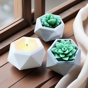 May include: Three geometric concrete planters, two with faux succulents and one with a white candle. The planters are all white with a geometric design.