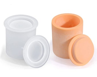 May include: Two silicone molds for making candles. One mold is white and the other is peach. Both molds have a cylindrical shape with a removable lid.