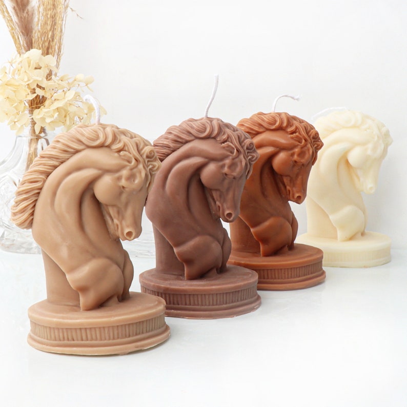 May include: Four decorative horse head candles in different shades of brown and white. The candles are sculpted in a realistic style and are arranged in a row on a white surface.