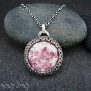 Puede incluir: Un collar de cadena de plata con un colgante que presenta una piedra redonda de color rosa y blanco encerrada en una jaula de alambre de plata.