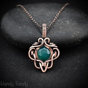 May include: A copper-colored pendant necklace with a dark green gemstone. The pendant has an intricate, wire-wrapped design with a central, faceted stone. The necklace chain is a dark, gunmetal color. The text "Handy Trendy" is at the bottom.