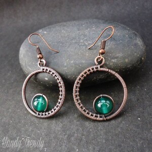 May include: Copper wire earrings with a green glass bead in the center of each circle.