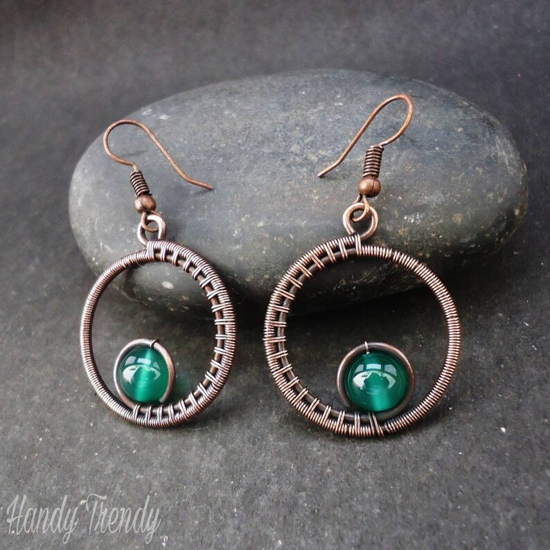 May include: Copper wire earrings with a green glass bead in the center of each circle.