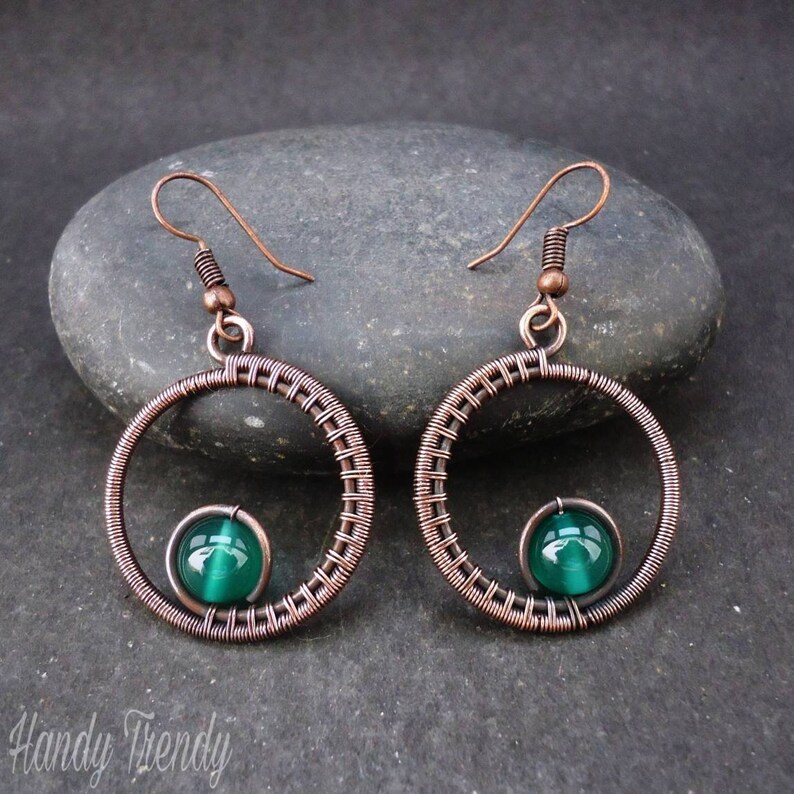 May include: Copper wire earrings with a green glass bead in the center of each circle.