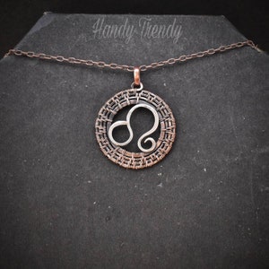 May include: A silver Leo zodiac sign pendant necklace with a copper wire frame. The necklace is on a black background.