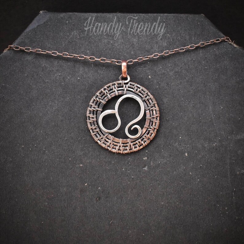 May include: A silver Leo zodiac sign pendant necklace with a copper wire frame. The necklace is on a black background.