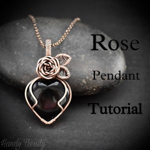 May include: A copper wire wrapped heart pendant with a black stone in the center. A copper wire rose with leaves sits on top of the heart. The pendant is on a chain and resting on a gray stone. The text "Rose Pendant Tutorial" is written below the pendant.