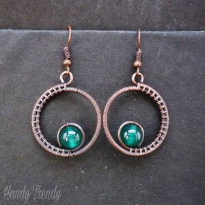 May include: Copper wire earrings with a green glass bead in the center of each hoop.