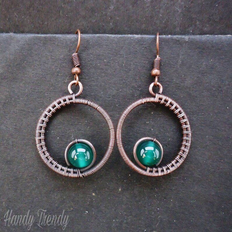 May include: Copper wire earrings with a green glass bead in the center of each hoop.