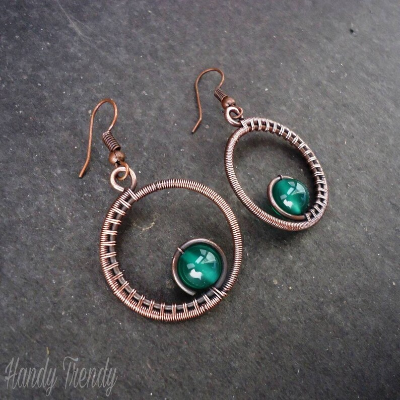 May include: Copper wire earrings with a green gemstone in each. The earrings are in the shape of a circle with a smaller circle inside.