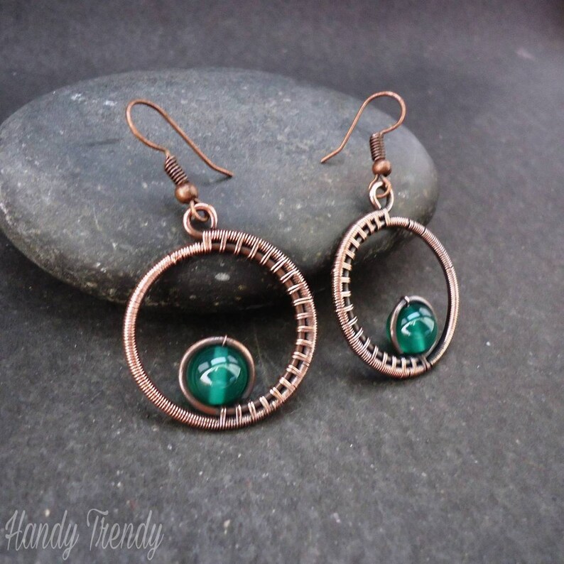 May include: Copper wire earrings with a green gemstone in the center of each circle.