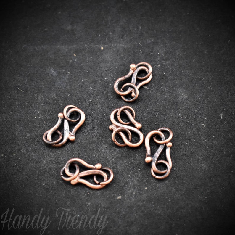 May include: Six copper-toned metal clasps with a decorative swirl design. The clasps are ideal for jewellery making or other craft projects.