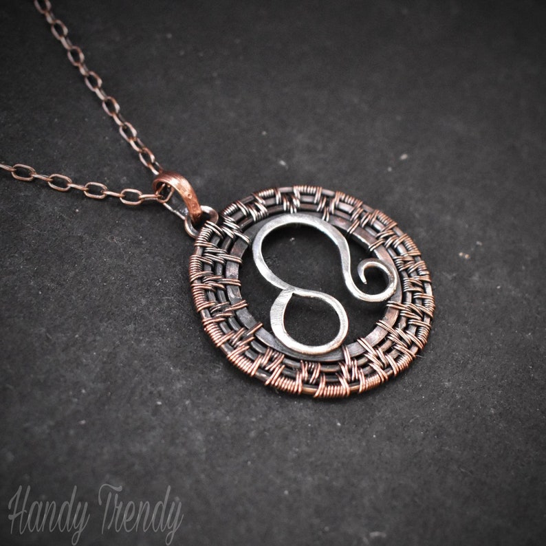May include: A silver Leo zodiac sign pendant with a copper wire woven frame, hanging from a silver chain.