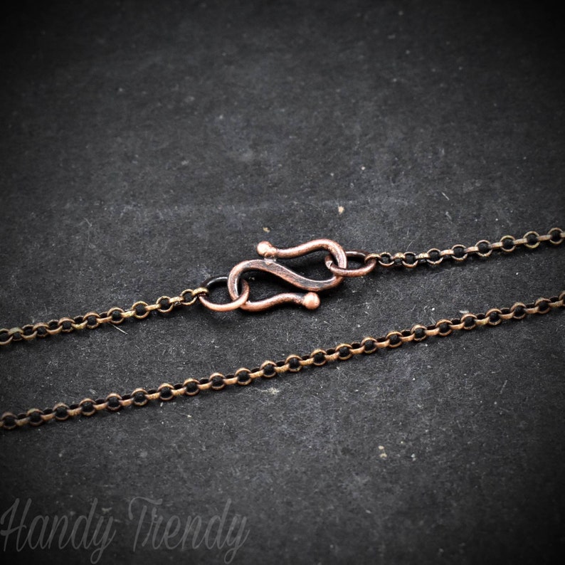 May include: A close-up of a copper-toned chain necklace with a lobster clasp closure. The chain is made of small, round links.