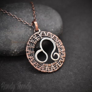 May include: A copper wire-wrapped pendant necklace featuring the Leo zodiac sign. The pendant is circular and has a silver Leo symbol inside.