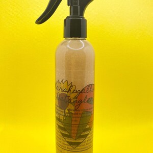 K&ouml;nnte beinhalten: Eine klare Flasche mit einer schwarzen Spr&uuml;hd&uuml;se, gef&uuml;llt mit einer goldenen Fl&uuml;ssigkeit. Die Flasche hat ein Etikett mit dem Text "Marshmallow Detangler" und einer Sonnenblumengrafik. Das Etikett listet auch die Zutaten auf, darunter Avocado&ouml;l, Lavendel&ouml;l, Zitronen&ouml;l und Pfefferminz&ouml;l.