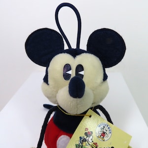 May include: A plush Mickey Mouse toy with a red and black outfit. The toy has a loop on top of its head and a tag that says "Mickey & Co."