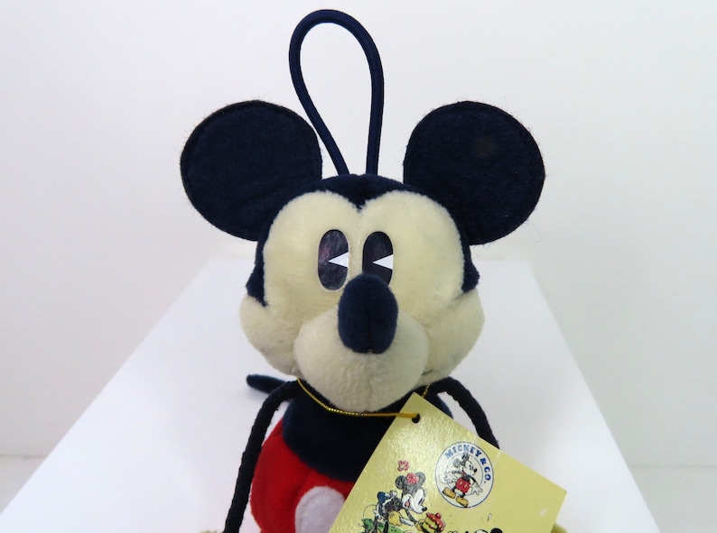 May include: A plush Mickey Mouse toy with a red and black outfit. The toy has a loop on top of its head and a tag that says "Mickey & Co."