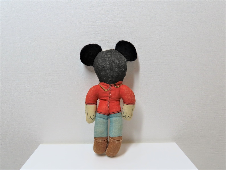K&ouml;nnte beinhalten: Eine Vintage-Stoffpuppe von Mickey Mouse mit schwarzen Ohren, einem roten Hemd, einer blauen Jeans und braunen Stiefeln.