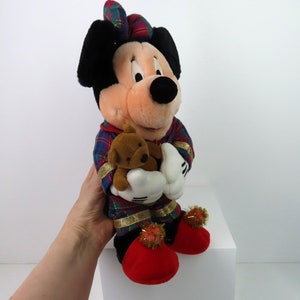 May include: A plush Mickey Mouse wearing red and green plaid pajamas and holding a brown teddy bear. He has red shoes with gold trim and pom-poms.