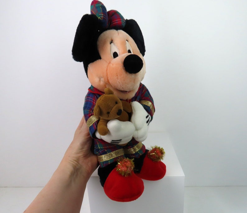 May include: A plush Mickey Mouse wearing red and green plaid pajamas and holding a brown teddy bear. He has red shoes with gold trim and pom-poms.