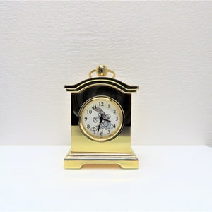 May include: A gold-colored tabletop clock with a white face and black hands. The clock features a Bugs Bunny image and the numbers 1 through 12.