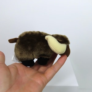 Könnte beinhalten: Ein braunes Plüschtier in Form eines Mini-Büffels mit einem cremefarbenen Horn. Das Spielzeug sitzt in der Hand einer Person.