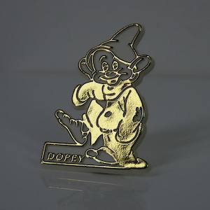 Può includere: Spilla in metallo dorato con un'immagine di cartone animato di Dopey da Biancaneve e i Sette Nani della Disney. La spilla ha uno sfondo bianco e la parola "Dopey" è scritta sulla base.
