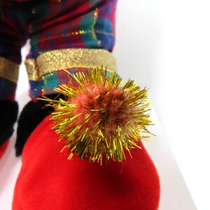 May include: Red and green plaid fabric with gold trim and a red fuzzy pom-pom with gold tinsel.