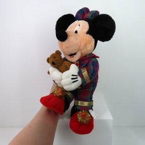 May include: A plush Mickey Mouse wearing red and green plaid pajamas and holding a brown teddy bear. He is wearing red slippers with gold trim and white pom-poms.